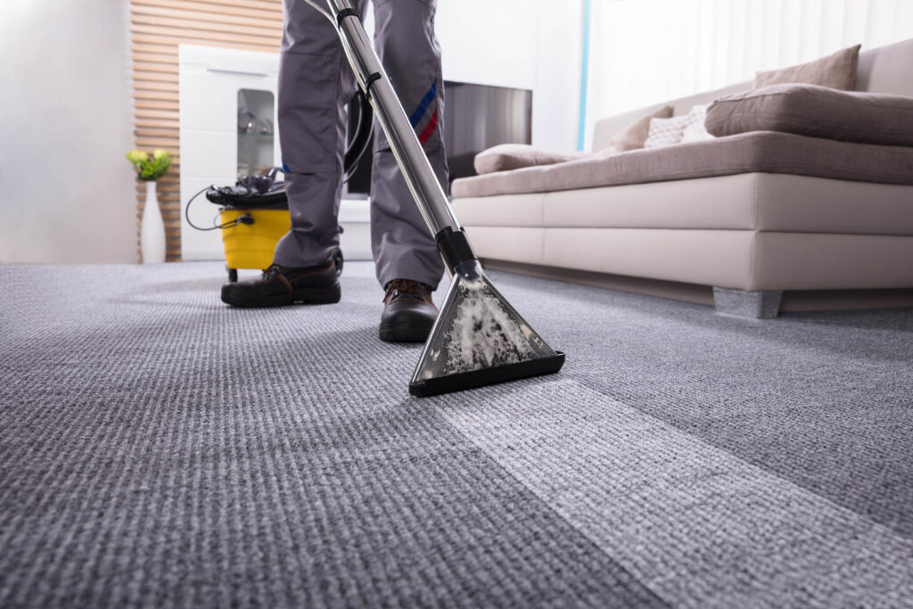 Low Section Of A Person Cleaning The Carpet With Vacuum Cleaner In Living Room