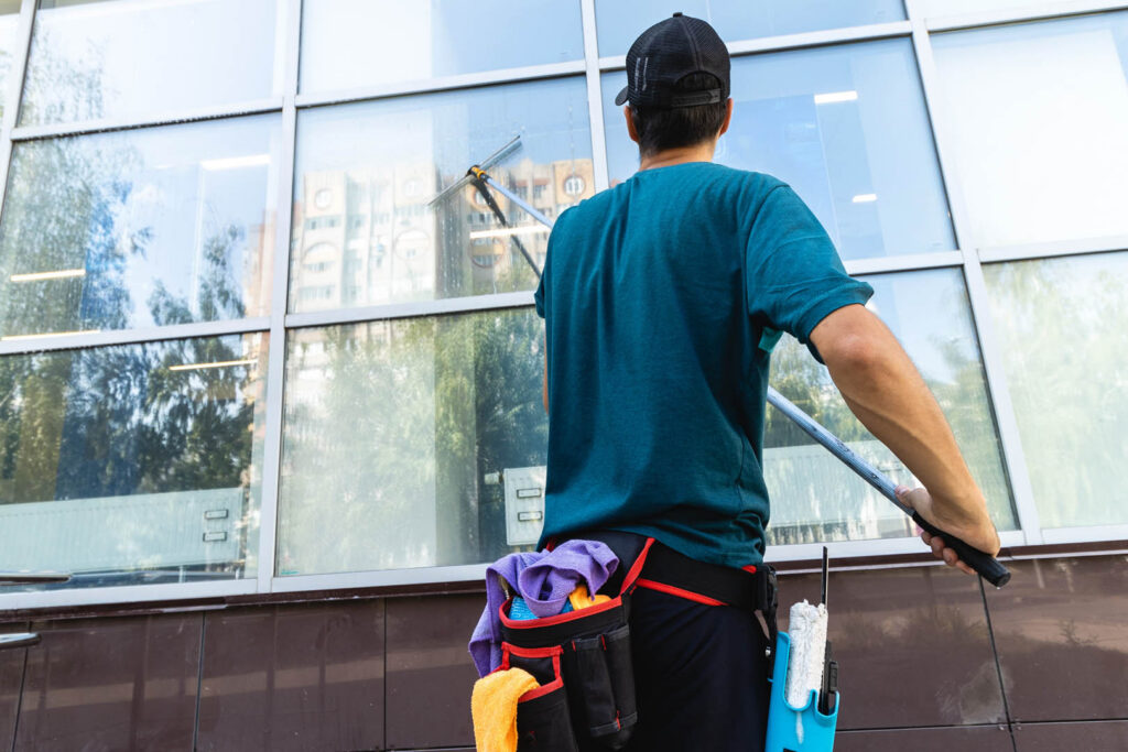 An employee of a professional cleaning service in overalls washes the facade and windows with special devices.